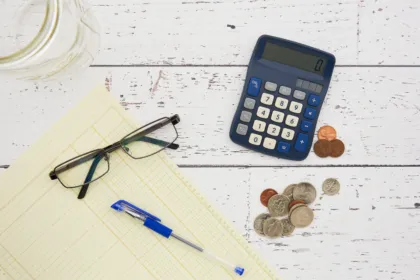 Calculator, coins, glasses and a ledger sheet used to plan a 50/30/20 budget