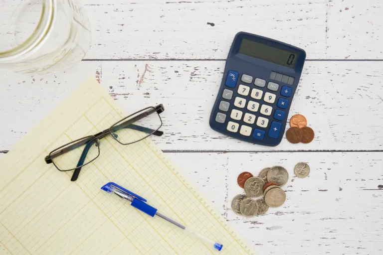 Calculator, coins, glasses and a ledger sheet used to plan a 50/30/20 budget