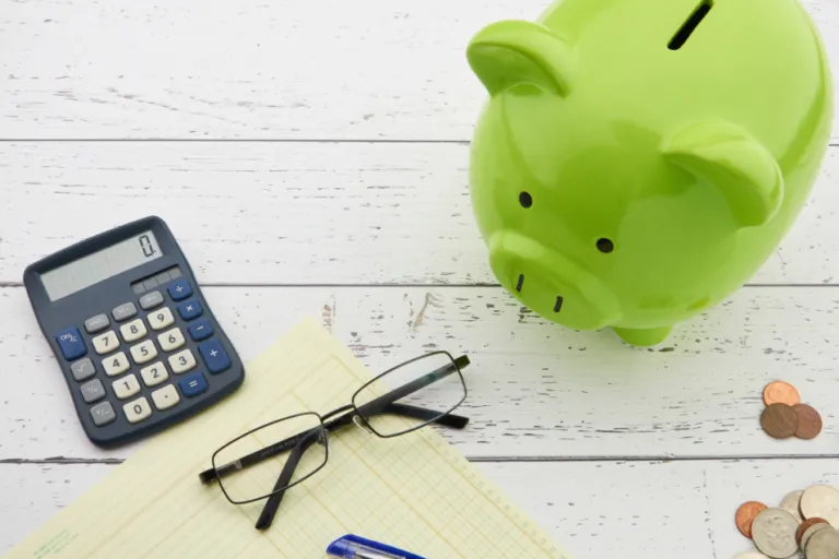 Green piggy bank with a calculator, coins and glasses for building an emergency fund