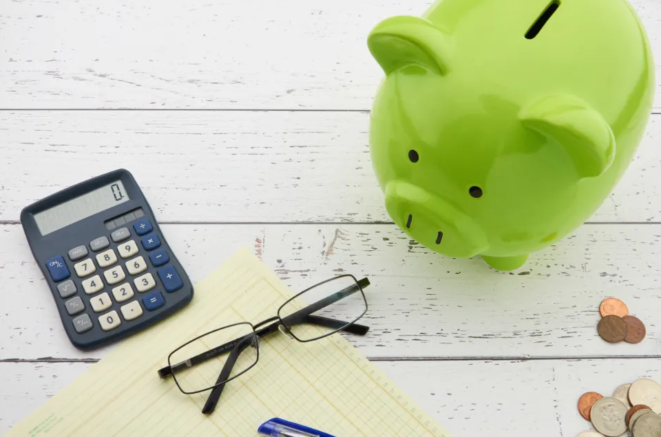 Green piggy bank with a calculator, coins and glasses for building an emergency fund