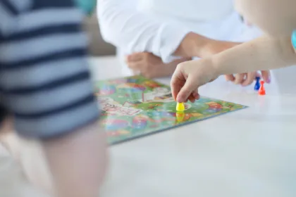 Child moving a yellow game piece on a colorful board during family game night