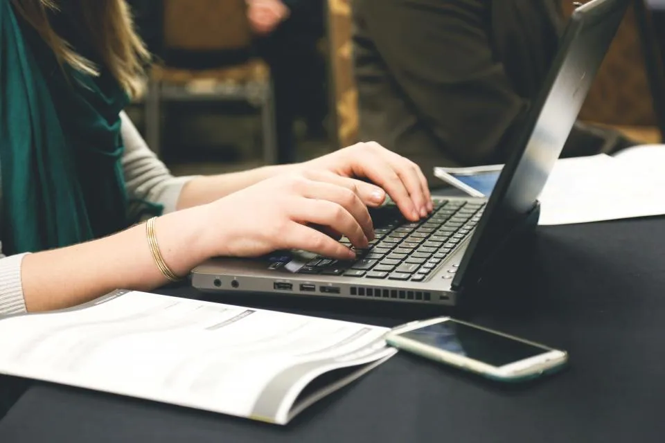 Person typing on a laptop while checking email for phishing warning signs