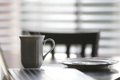 Steaming coffee mug and breakfast plate on a table in soft morning light