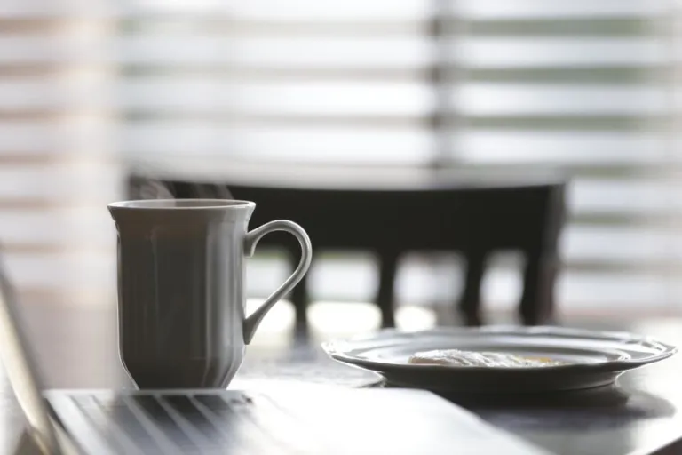 Steaming coffee mug and breakfast plate on a table in soft morning light