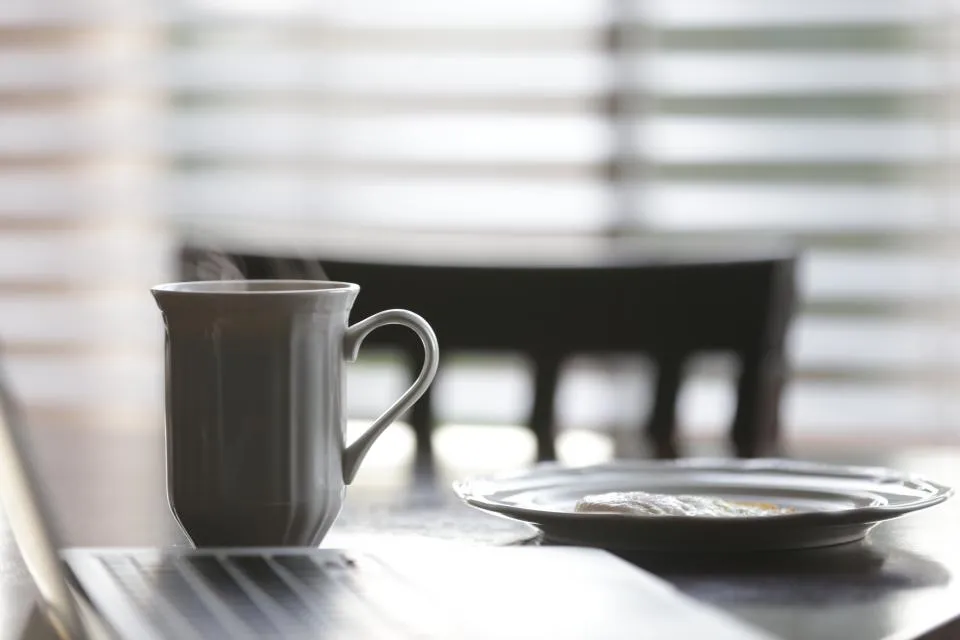 Steaming coffee mug and breakfast plate on a table in soft morning light