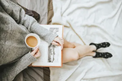 Person reading an open book with a cup of coffee on a cozy bed