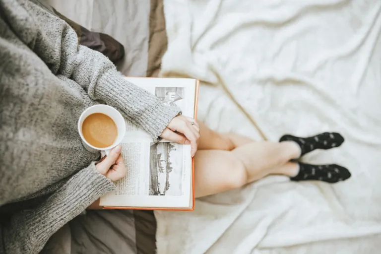 Person reading an open book with a cup of coffee on a cozy bed