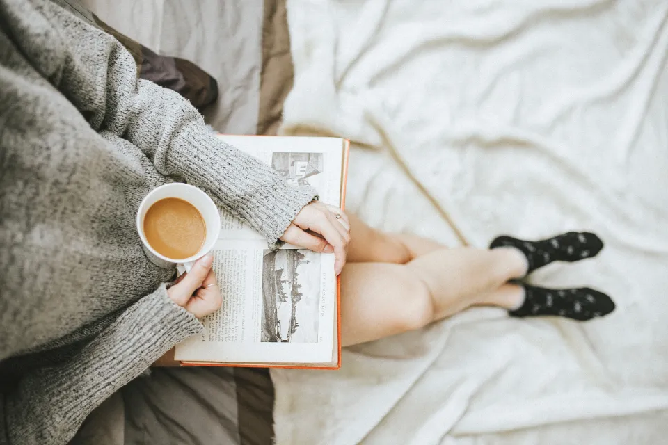 Person reading an open book with a cup of coffee on a cozy bed